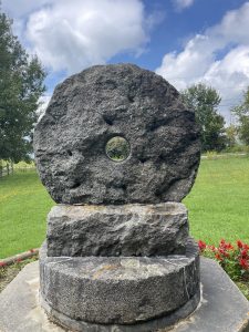 Millstone for grinding grains standing on edge with hole in middle resting atop another millstone.